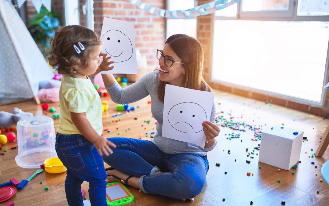 Young beautiful psicologist and toddler doing therapy using emoji emotions at kindergarten